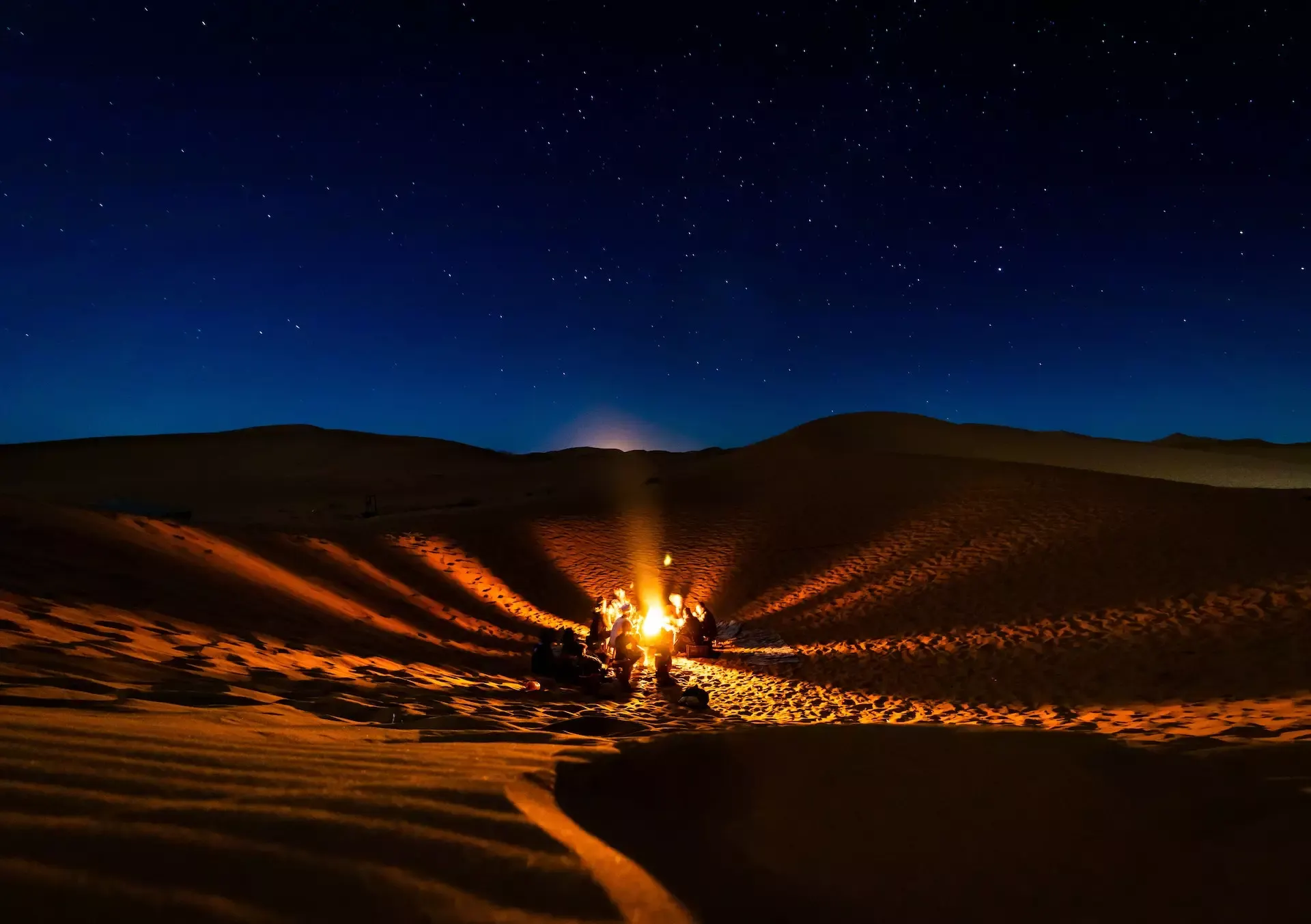 Viajeros reunidos alrededor de una hoguera bajo el cielo estrellado del desierto